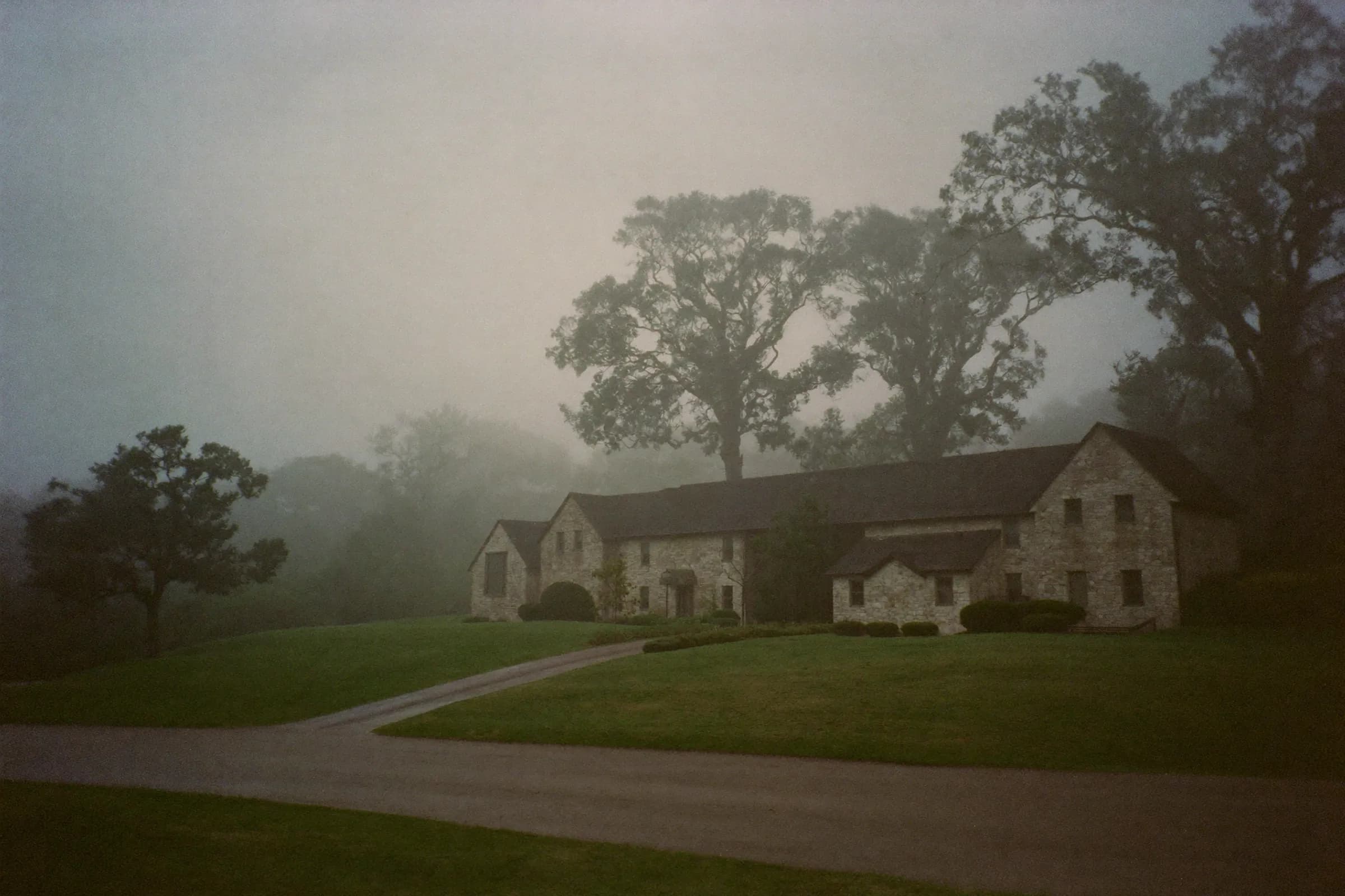 A stone estate house among oaks in morning fog