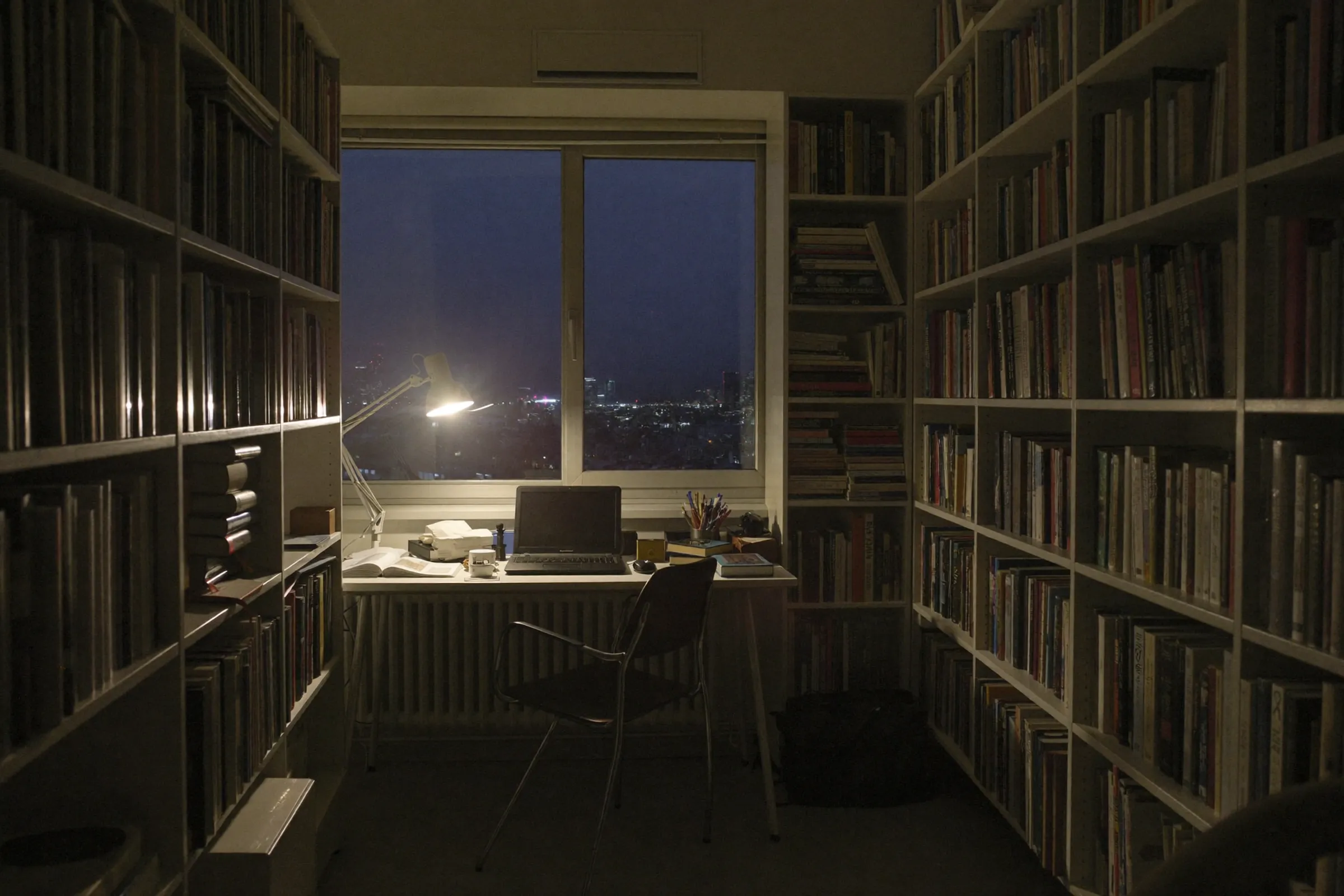 A private study with bookshelves and a city view at night